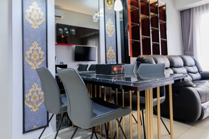 Una sala de estar moderna con zona de comedor, que incluye un sofá de cuero negro, una mesa de comedor con sillas y un televisor montado en la pared.