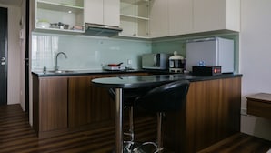 A kitchen with a bar stool, a refrigerator, a microwave, and a sink. - City View Studio Apartment at Tamansari La Grande (Bandung)