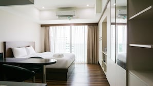 A hotel room with a bed, a desk, a chair, a mirror, and a window with curtains. - City View Studio Apartment at Tamansari La Grande (Bandung)