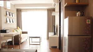 A modern kitchen with a refrigerator, a dining table, and a sofa. There is a window with curtains and a view of the outside. - Classic 2BR Apartment At Gateway Pasteur near Exit Toll (Cimahi)