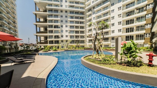 A swimming pool with blue mosaic tiles, surrounded by lounge chairs and plants, with high-rise buildings in the background. - Classic 2BR Apartment At Gateway Pasteur near Exit Toll (Cimahi)
