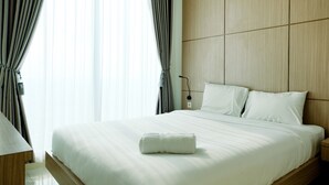 A neatly made bed with a rolled towel, wooden headboard, and a bedside table with a lamp. - Comfortable 1BR Tree Park Apartment (South Tangerang)