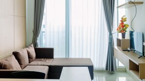 A modern living room with a sofa, a coffee table, and a TV on a stand. - Comfortable 1BR Tree Park Apartment (South Tangerang)