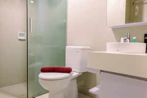 A modern bathroom with a glass shower enclosure, a white toilet, and a sink with toiletries. - Comfortable 1BR Tree Park Apartment (South Tangerang)