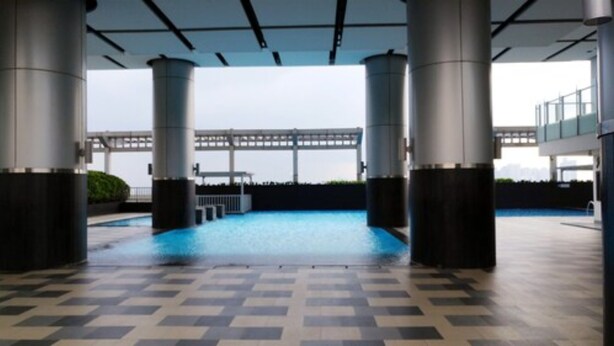 A covered swimming pool with a checkered floor, surrounded by columns, and a view of a bridge in the background.