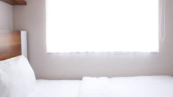 Un lit simple avec une tête de lit en bois, un oreiller blanc et une fenêtre ornée d’un rideau léger.