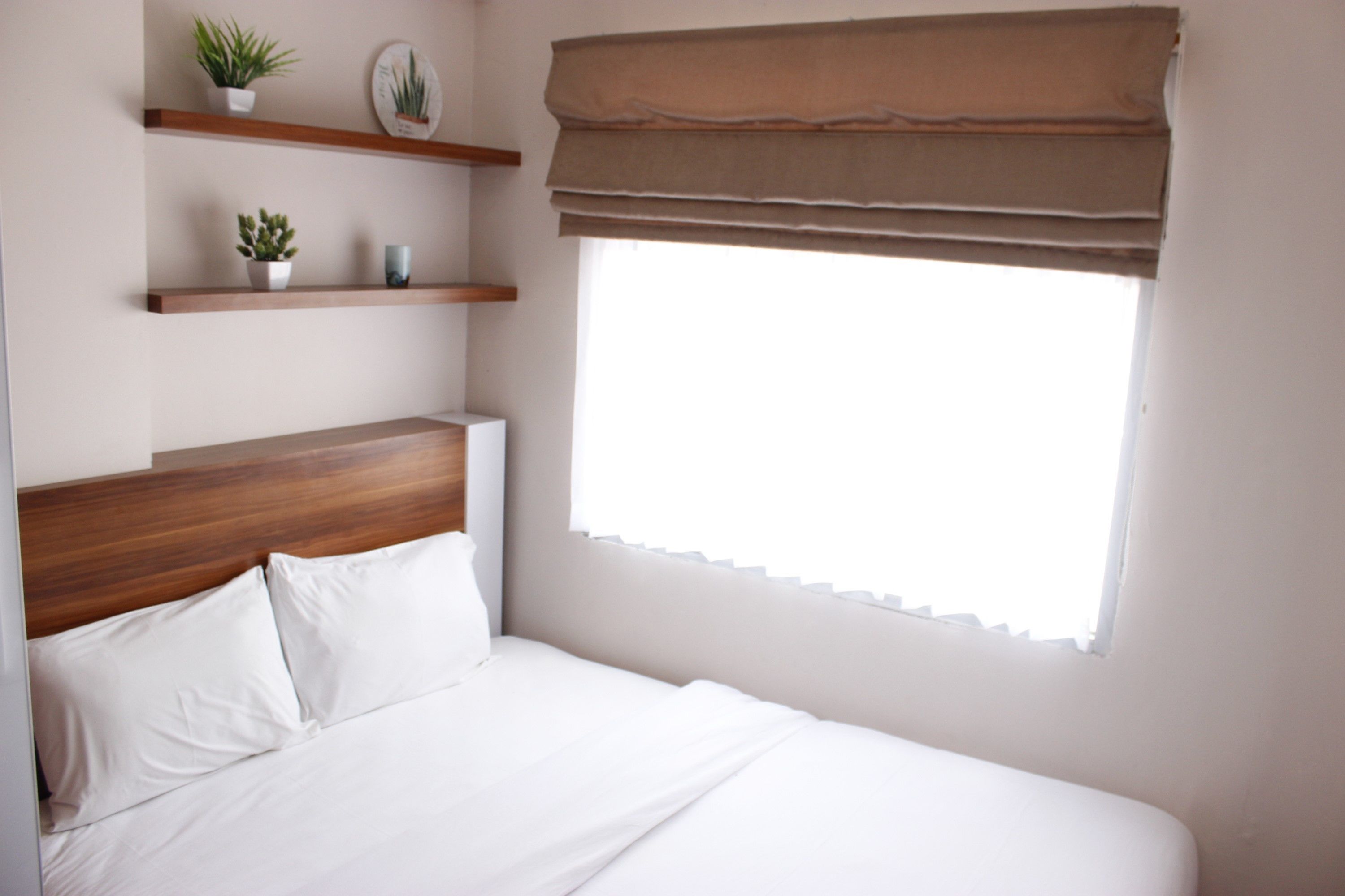 A neatly made bed with white linens, a wooden headboard, and a window with a brown valance.