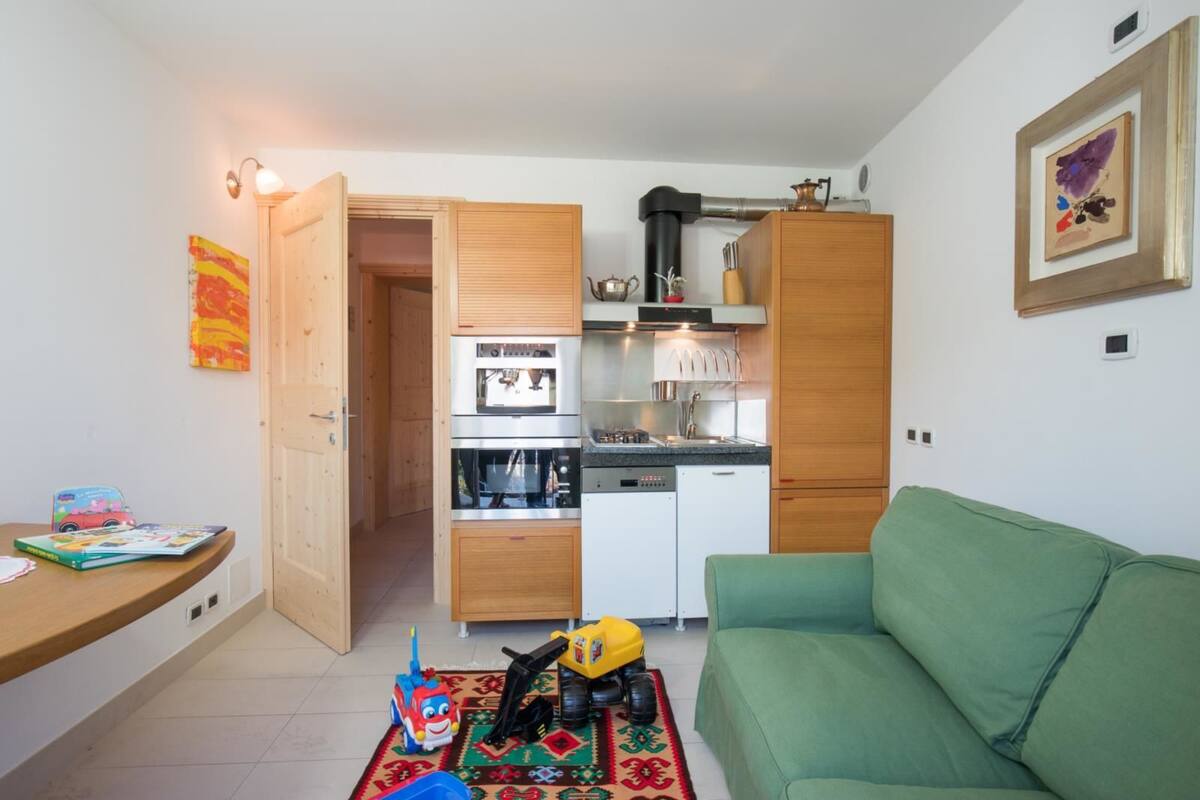 A compact living space with a kitchenette, a green sofa, and a child's toy on the floor.