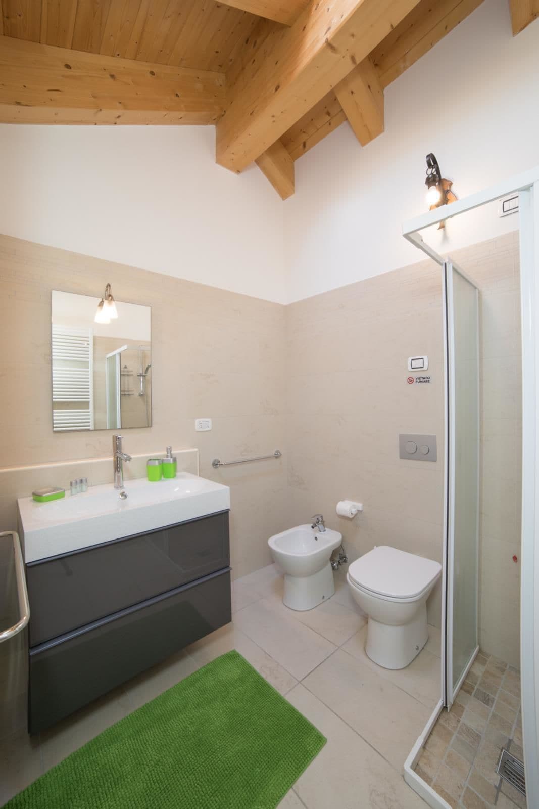 Un baño moderno con techo de madera, un espejo grande, un lavabo con tocador, un bidé, un inodoro y una zona de ducha.