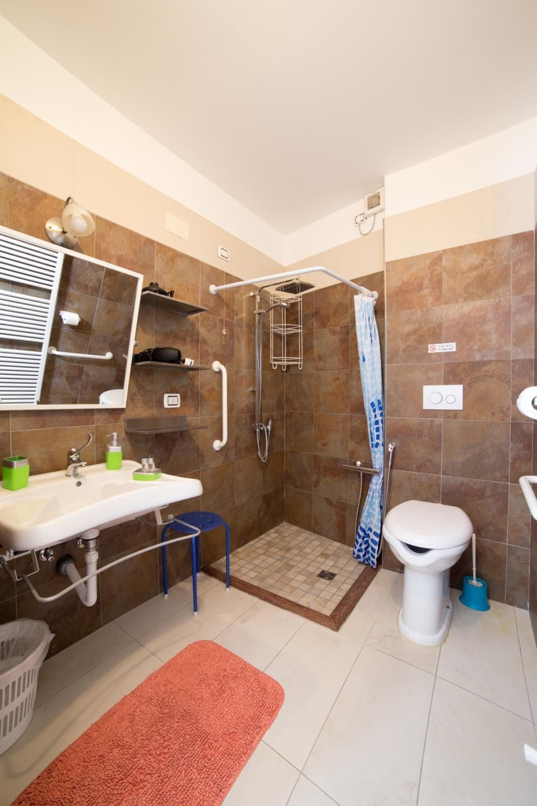 Baño con ducha, inodoro, lavabo y un taburete pequeño.