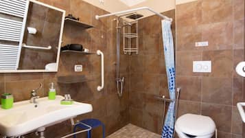 Baño con ducha, inodoro, lavabo y un taburete pequeño.