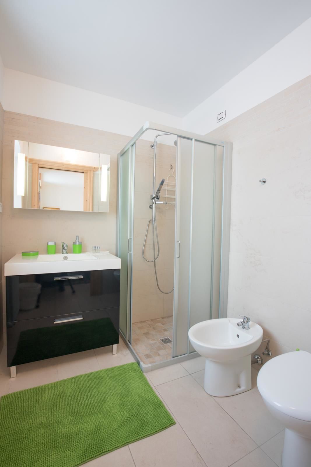 Uma casa de banho moderna com chuveiro de parede de vidro, toucador com espelho e lavatório independente.