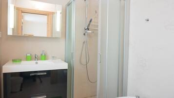 Uma casa de banho moderna com chuveiro de parede de vidro, toucador com espelho e lavatório independente.