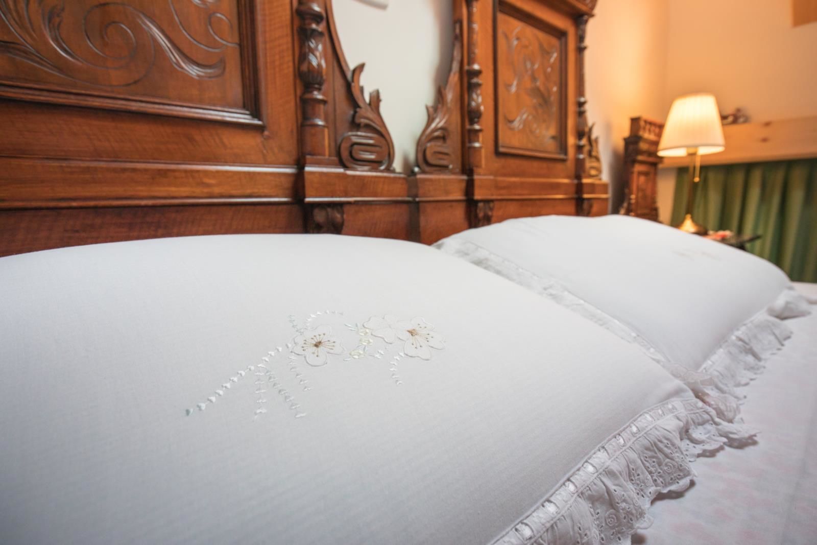 Un letto con lenzuola bianche e ricami floreali, una testiera in legno e una tenda verde sullo sfondo.