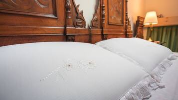 Un letto con lenzuola bianche e ricami floreali, una testiera in legno e una tenda verde sullo sfondo.