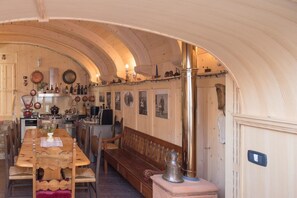 Un interior acogedor de madera con una larga mesa de comedor, bancos y una estufa central.