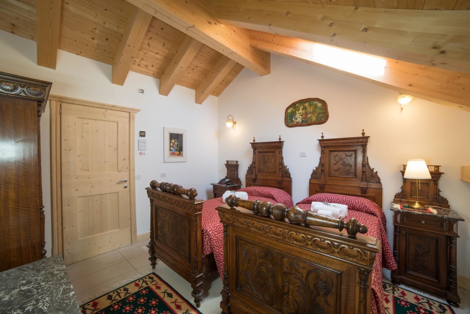 A traditional bedroom with wooden furniture, a bed with red and white bedding, a wooden door, and a small table with a lamp.