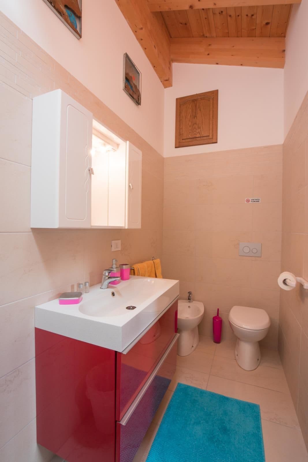 A bathroom with a white sink, red cabinet, wooden ceiling, and a blue rug.