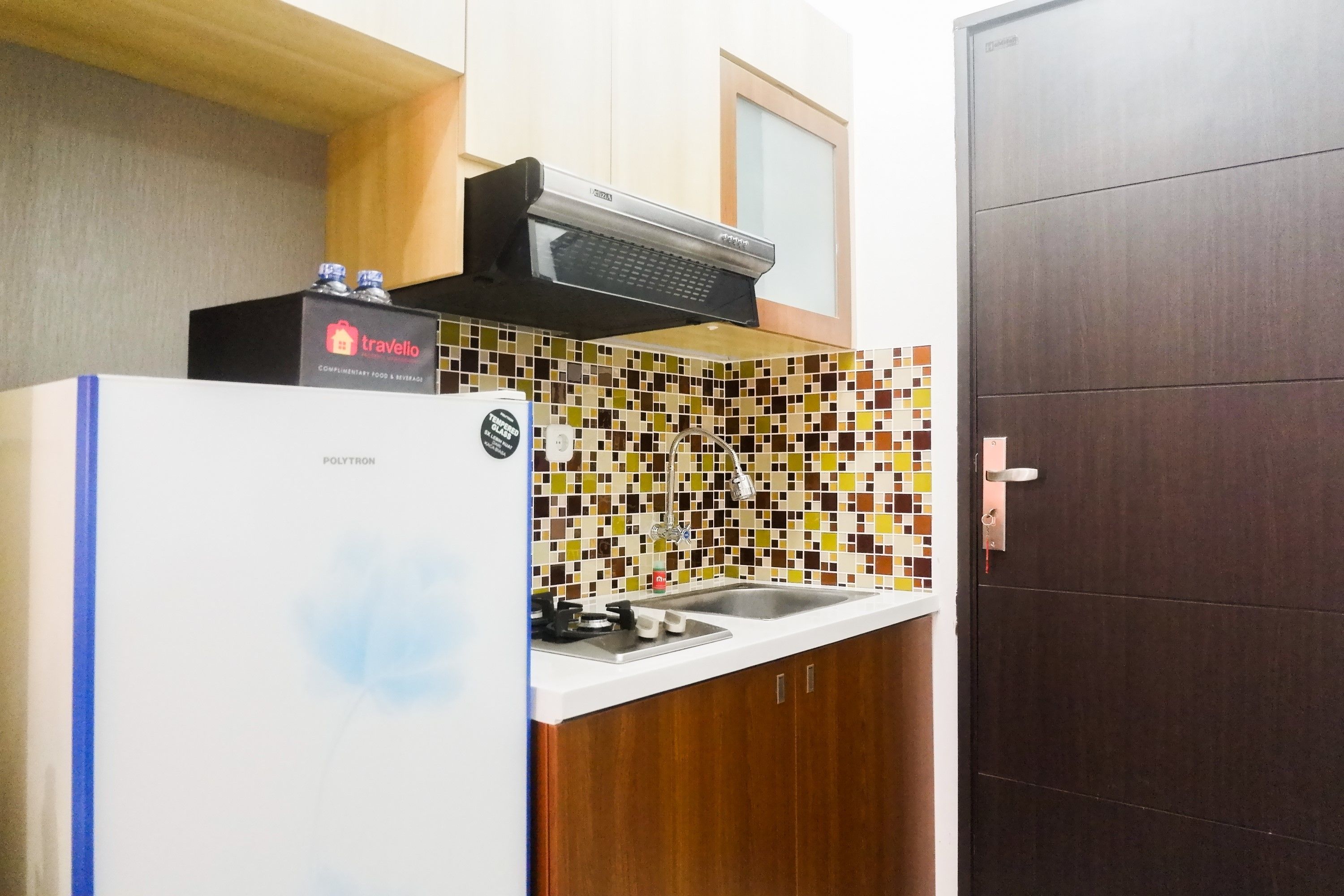 A compact kitchen with a white refrigerator, a microwave, and a sink. The backsplash features a mosaic tile pattern.