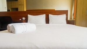 A neatly made bed with white linens and pillows, a rolled white towel, and a wooden headboard. - Comfy Studio Apartment at Menara Rungkut (Surabaya)