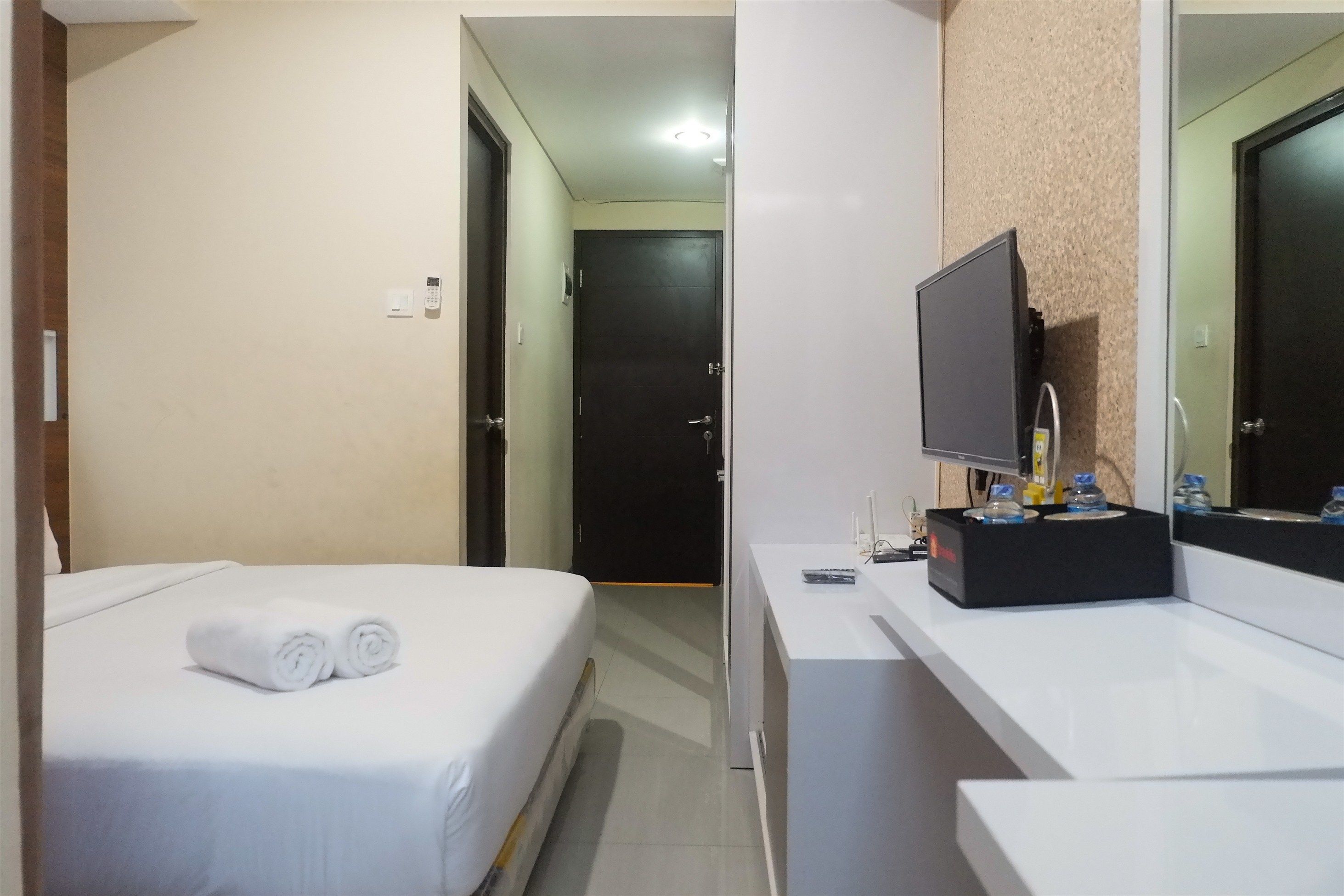 A hotel room with a bed, a TV, a bathroom with a mirror, and a sink.