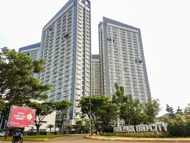 Un immeuble résidentiel de grande hauteur, doté de nombreux balcons, entouré de verdure et agrémenté d’un panneau indiquant la proximité d’une zone commerciale.