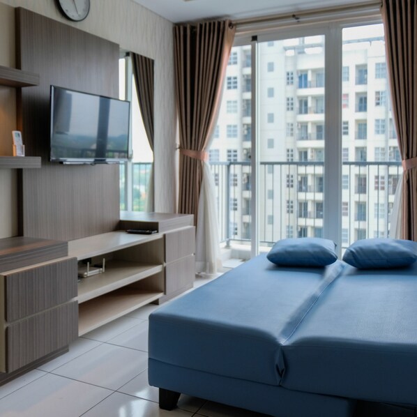 A modern bedroom with a bed, a TV, and a balcony with a city view.