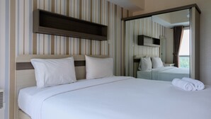 A hotel room with a large bed, a wooden headboard, a mirror, and striped wallpaper. - Cozy 1BR at Casa De Parco Apartment (Pagedangan)