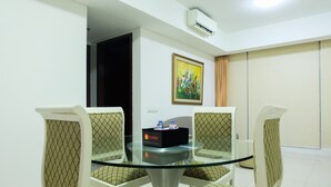 A conference room with a glass table surrounded by four patterned chairs, a painting on the wall, and an air conditioning unit above. - Cozy and Elegant 2BR Kemang Village Apartment (Jakarta)