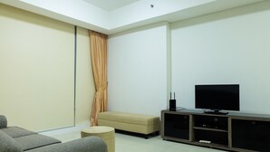 A living room with a sofa, ottoman, television, and entertainment unit. - Cozy and Elegant 2BR Kemang Village Apartment (Jakarta)