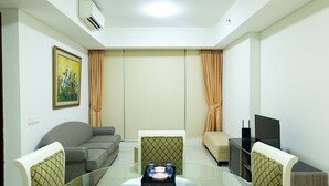 A modern living room with a glass coffee table, a sofa, a patterned armchair, a TV, and a painting on the wall. - Cozy and Elegant 2BR Kemang Village Apartment (Jakarta)
