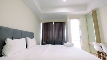 Habitación de hotel con una cama grande, un cabecero tapizado en gris, una mesita de noche con lámpara y una ventana con cortinas.