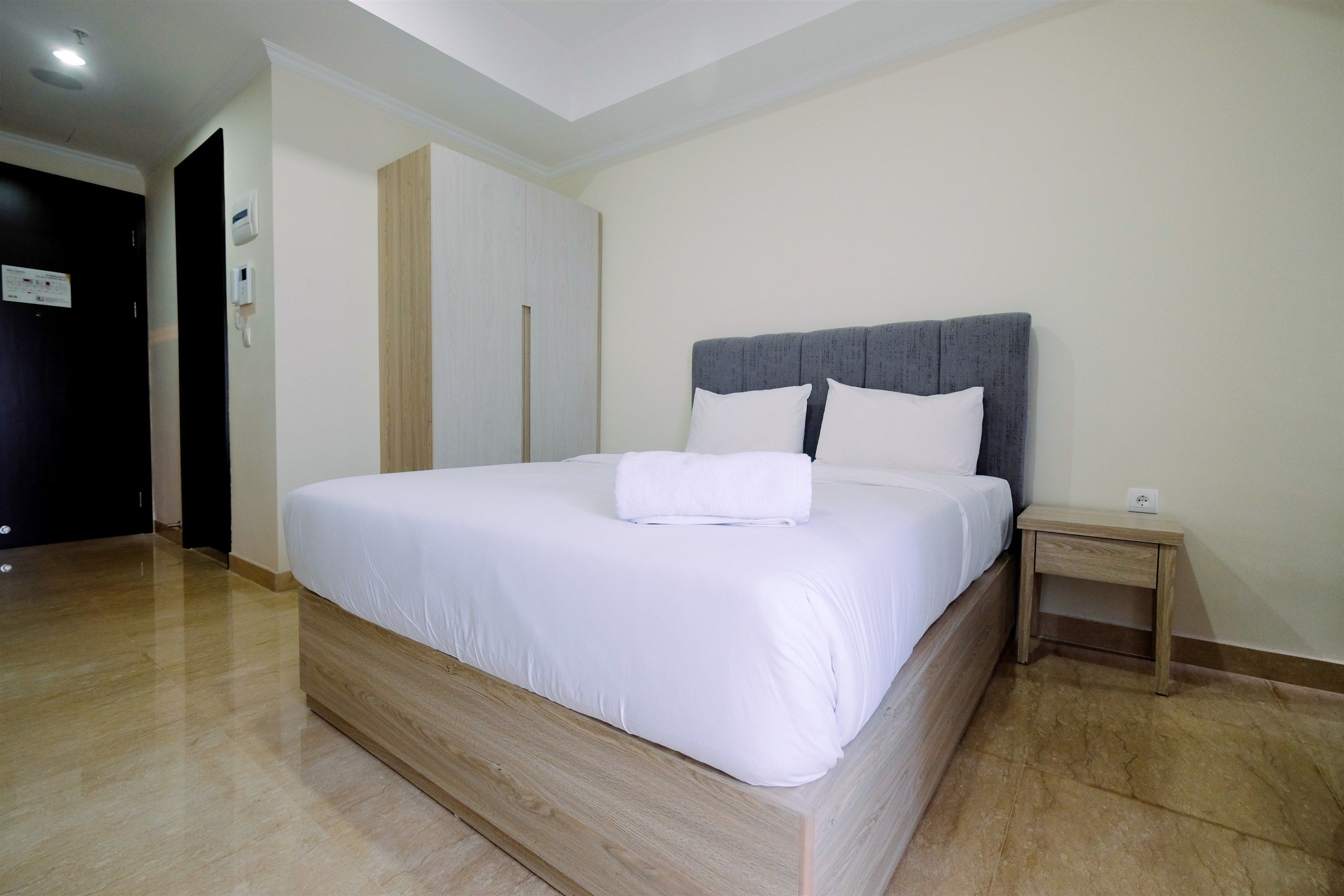 A modern hotel room with a large bed, a wooden headboard, a bedside table, and a wardrobe.