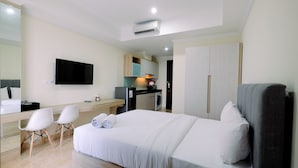 Quarto de hotel moderno com uma cama grande, uma escrivaninha com cadeira, televisão de tela plana e cozinha compacta.