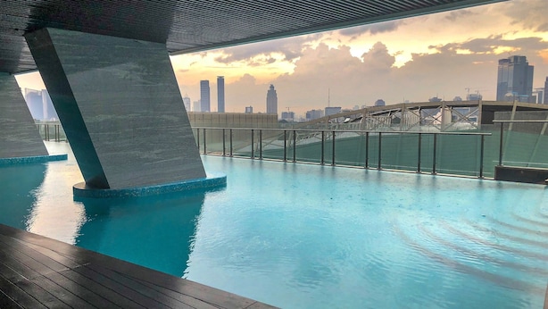 Piscina interna com vista para o horizonte urbano, um deck de madeira e uma estrutura de concreto acima.