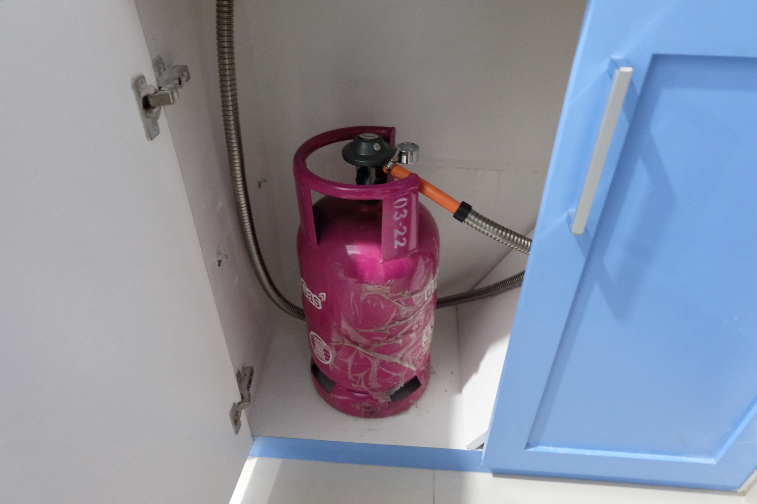 A pink gas cylinder with a hose attached, placed inside a blue cabinet.
