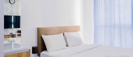A modern hotel room with a large bed, a bedside table, a mirror, and a window with curtains.