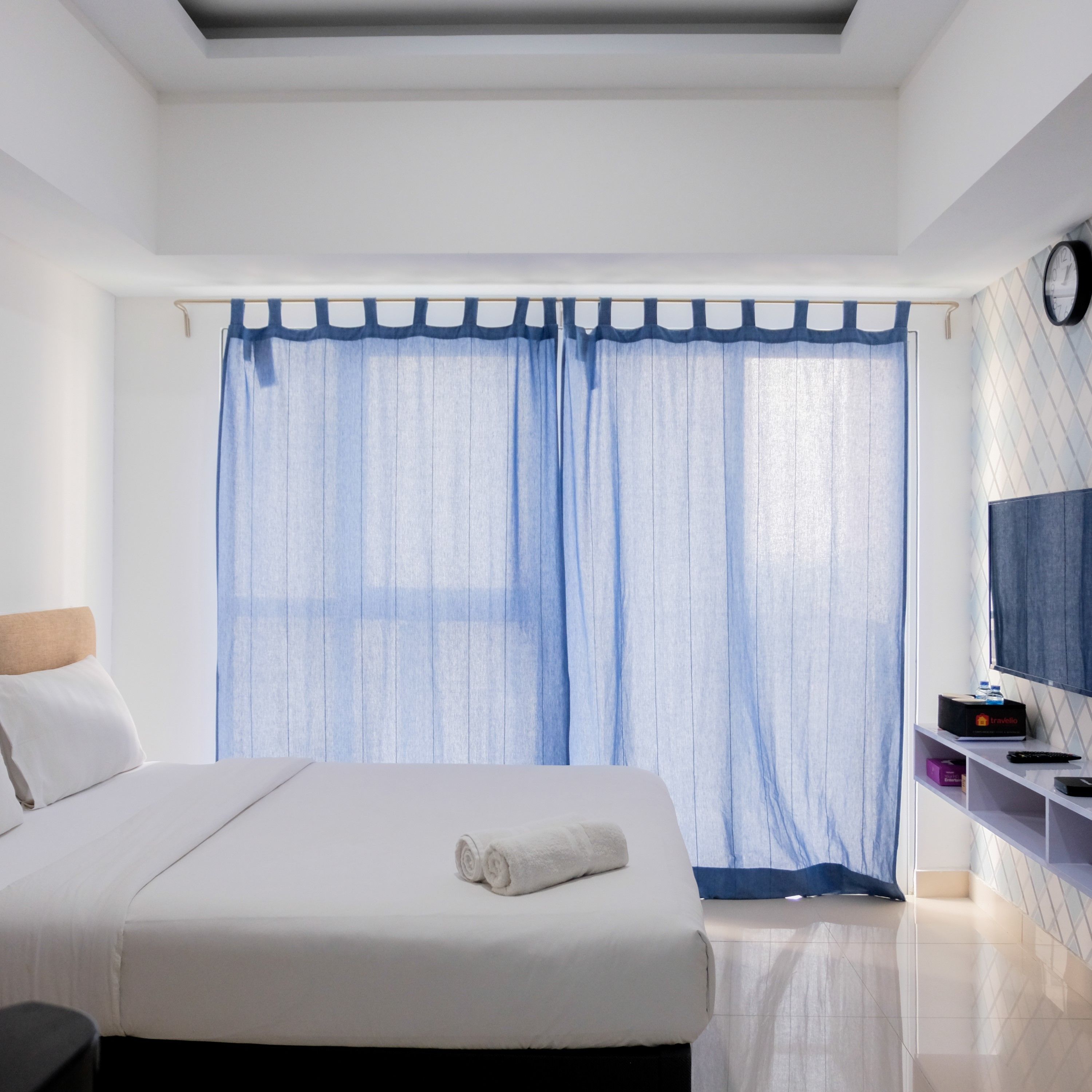 Une chambre d’hôtel moderne avec un grand lit, un téléviseur posé sur un meuble et une fenêtre agrémentée de rideaux légers.