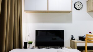 Een moderne hotelkamer met een bed, een televisie, een bureau, een stoel, een klok en een potplant.