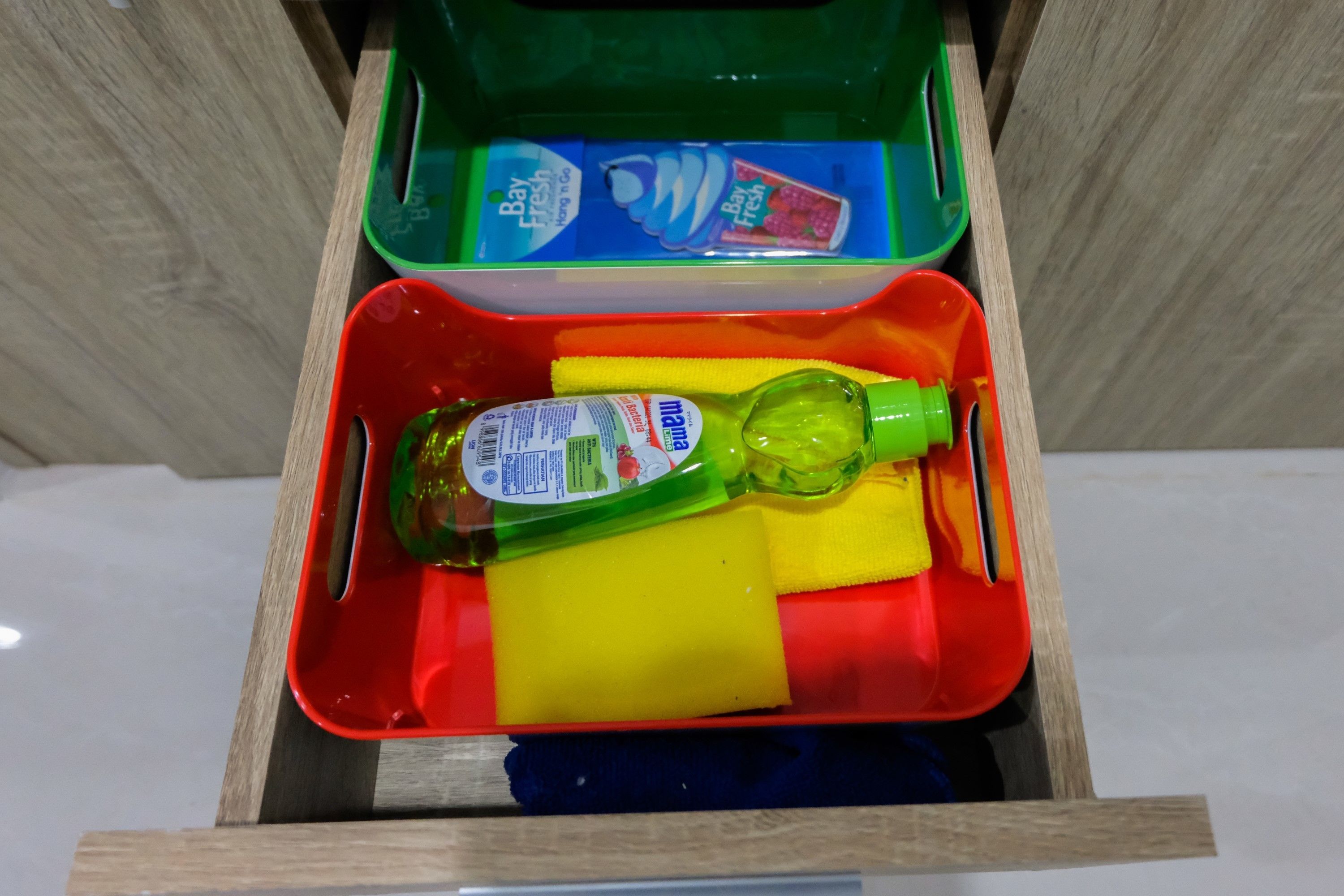 A drawer containing a green bottle, a yellow sponge, and a red container with a blue lid.