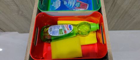 A drawer containing a green bottle, a yellow sponge, and a red container with a blue lid.