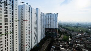 A high-rise building with multiple floors, a visible road, and a distant cityscape. - Elegant Studio Bassura Apartment (Jakarta)