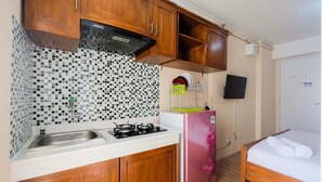 A compact kitchen with wooden cabinets, a tiled backsplash, a gas stove, and a pink refrigerator. - Elegant Studio Bassura Apartment (Jakarta)