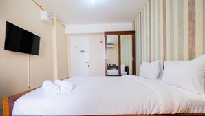 A hotel room with a wooden bed, white bedding, a flat-screen TV mounted on the wall, and a striped wallpaper on one wall. - Elegant Studio Bassura Apartment (Jakarta)