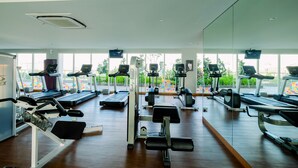 A gym with treadmills, weight machines, and a large window with a view of greenery.