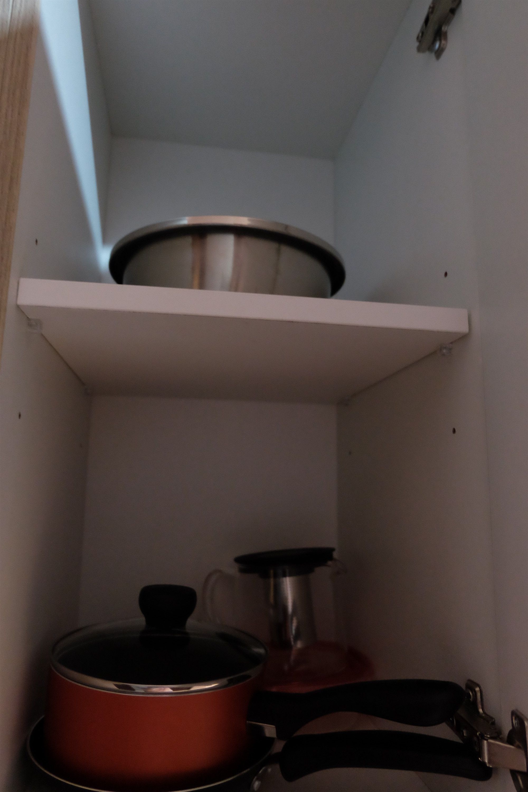 A kitchen with a white shelf holding a pot and a pan.