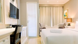 A hotel room with a bed, a desk with a chair, a television, and a window with curtains.