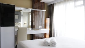 Une chambre d’hôtel avec un lit, un bureau, une chaise, un miroir et une fenêtre avec des rideaux.