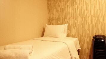 A neatly made bed with white linens and a rolled towel, a black heater, and a textured wall pattern.