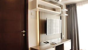 A modern living room with a flat-screen TV mounted on a wooden console, a dark wooden door, and a window with curtains. - Gorgeous 2BR Apartment at Gateway Pasteur near Exit Toll (Cimahi)